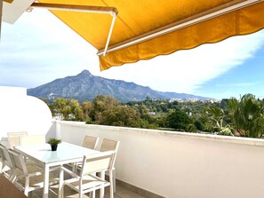 Eine Terrasse mit Tisch und Stühlen, einem gelben Sonnensegel und Blick auf die Berge.