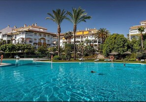Ein Swimmingpool mit Palmen und einem Hotelgebäude im Hintergrund.