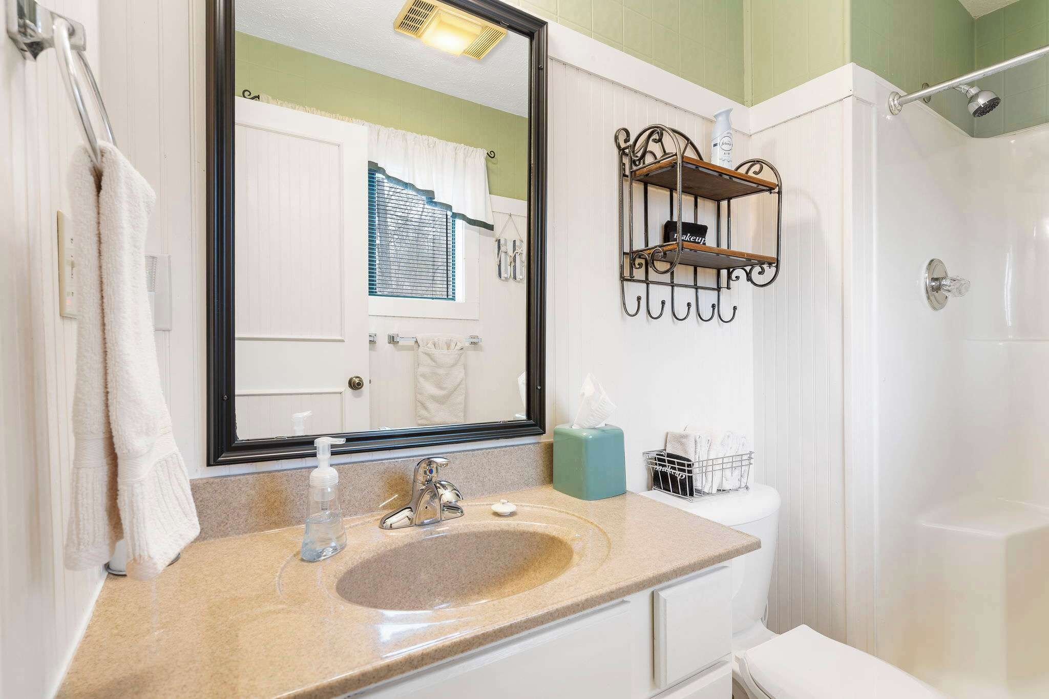 A bathroom with a sink, mirror, towel rack, and a shower area.