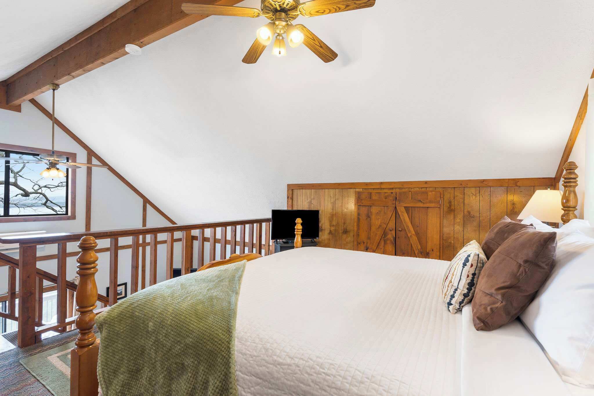 A bedroom with a wooden ceiling, a bed with a green blanket, and a wooden headboard.