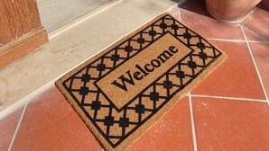 A welcome mat with a geometric pattern and the word "Welcome" in the center, placed on a tiled floor at the entrance of a building.