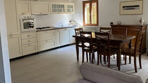 A kitchen with white cabinets, a dining table with chairs, and a window with blinds.