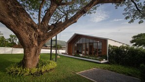 Ein modernes Haus mit einem großen Baum im Vordergrund, einem gepflegten Rasen und blauem Himmel.