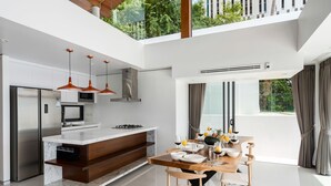 Une cuisine moderne dotée d’un îlot central, d’appareils électroménagers en acier inoxydable et de luminaires suspendus.