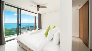 Une chambre moderne avec un grand lit, un ventilateur de plafond et une vue sur l’océan.