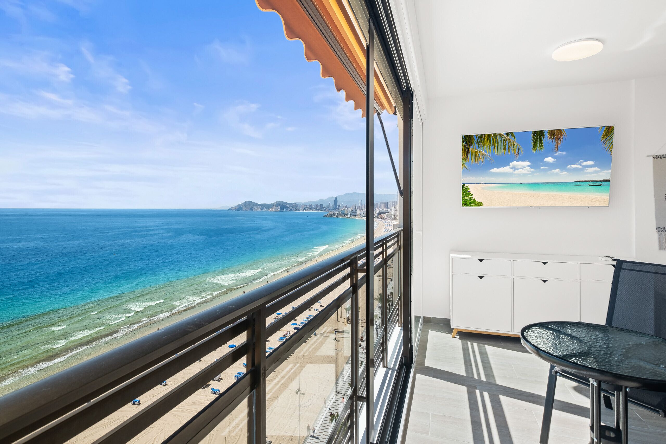 Un balcone con vista su spiaggia e oceano, un tavolo da pranzo e un quadro raffigurante una spiaggia.