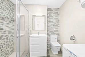 Un baño moderno con cabina de ducha de vidrio, un lavabo blanco y un inodoro.