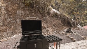A portable grill on a wheeled cart with a rocky and vegetated background. - Casa Lia  (San Isidro)