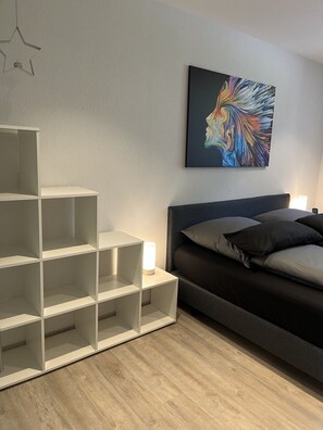A modern bedroom with a bed, a white shelving unit, and a colorful abstract painting on the wall.