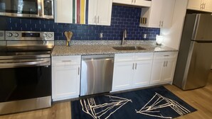 A modern kitchen with white cabinets, stainless steel appliances, and a blue backsplash. - Perfect beach Hideaway (Lewes)