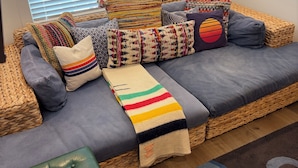 A cozy living room with a woven sofa, colorful cushions, a striped throw blanket, and a green ottoman. - Perfect beach Hideaway (Lewes)
