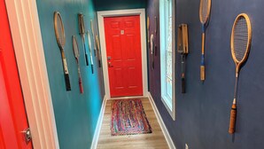 A hallway with a red door, wooden floors, and tennis rackets hanging on the walls. - Perfect beach Hideaway (Lewes)