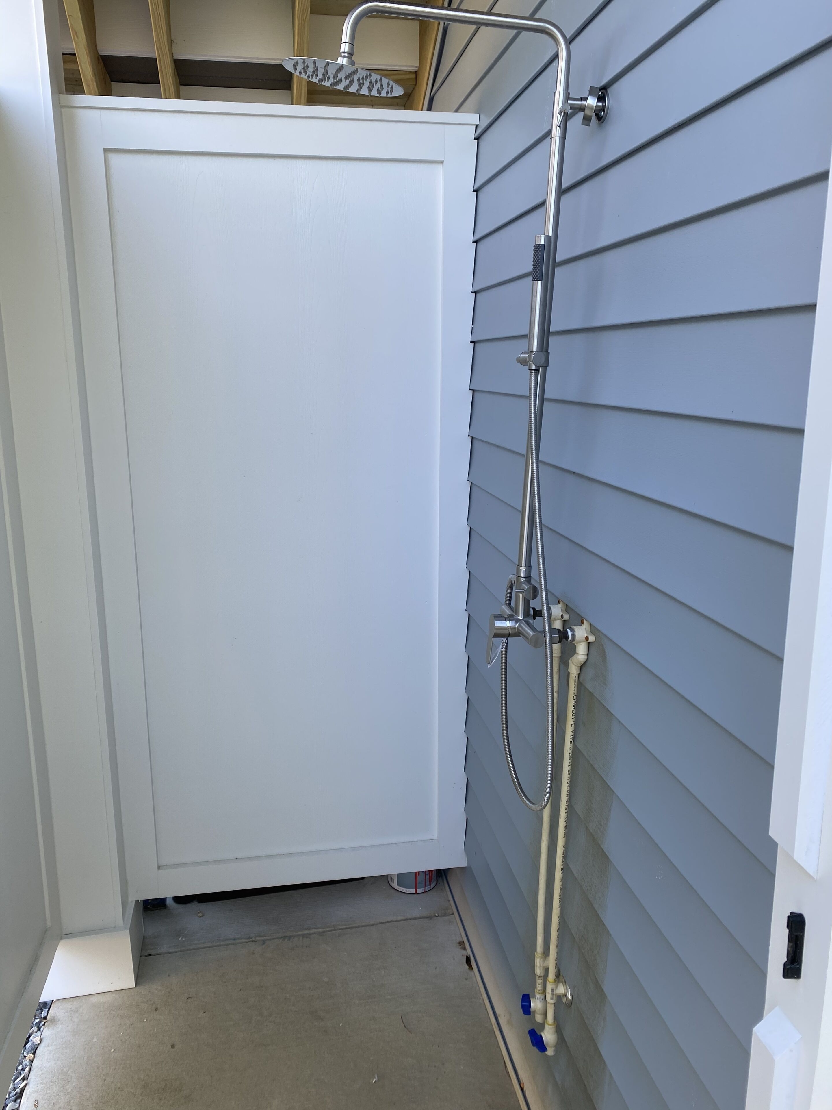 A small, enclosed shower area with a white door, a handheld showerhead, and a hose.