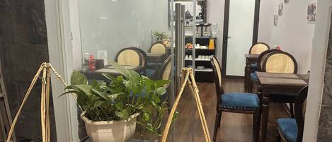 A modern dining area with glass partitions, wicker furniture, and a potted plant.