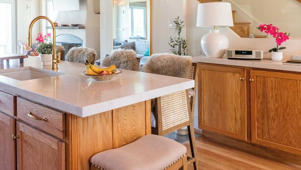 Une cuisine moderne avec des meubles en bois, un îlot central doté de tabourets et des luminaires suspendus.
