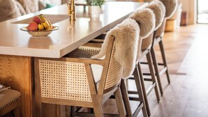 Une cuisine moderne avec un grand îlot central, des chaises en bois recouvertes de peaux de fourrure et des luminaires suspendus.