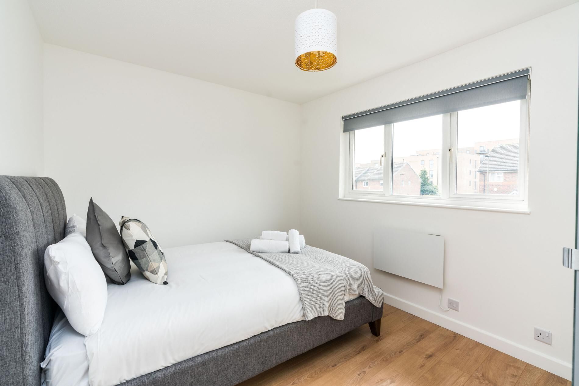 A bedroom with a bed, pillows, a window, and a radiator.