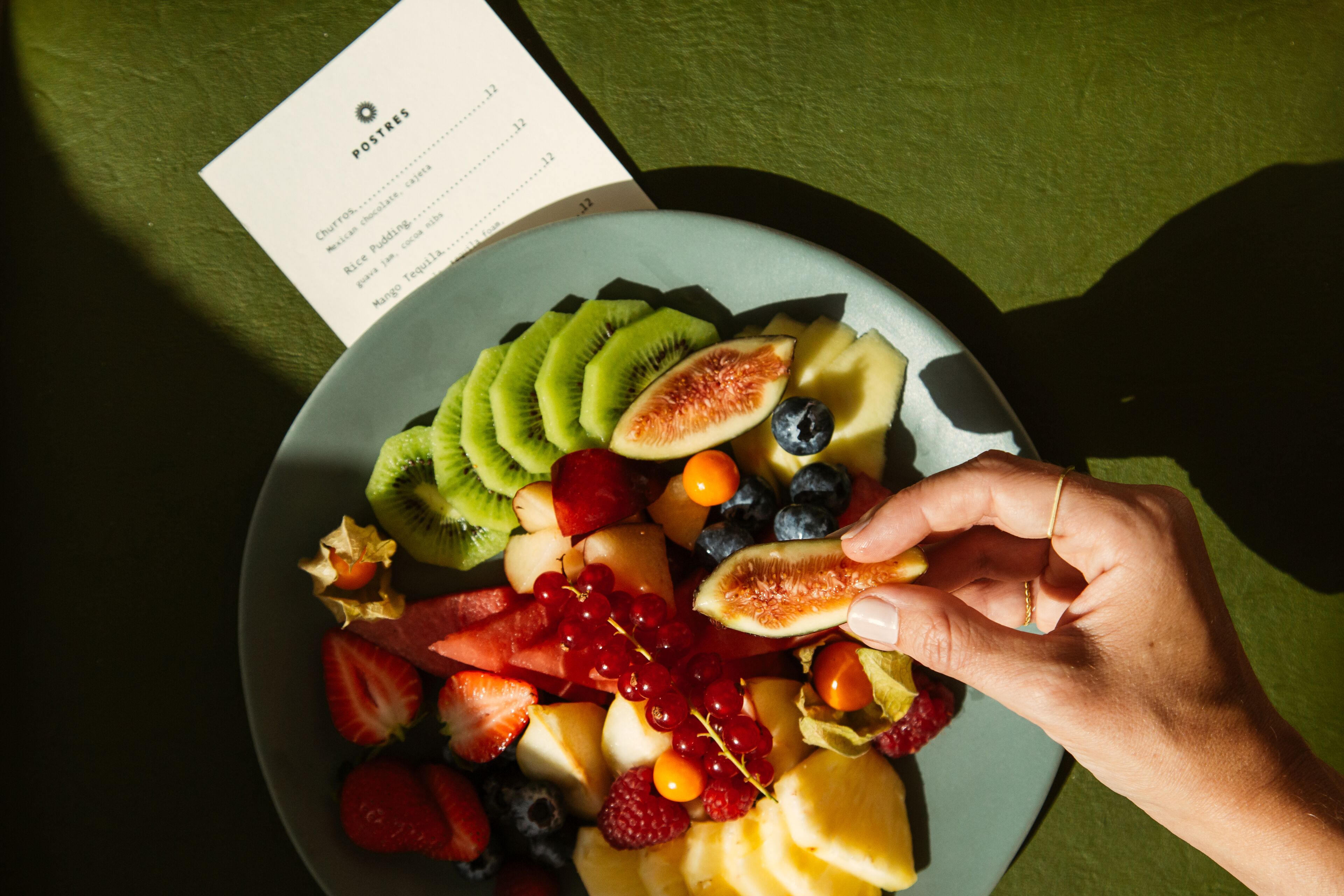 Un piatto di frutta mista con una mano che raccoglie una fetta.