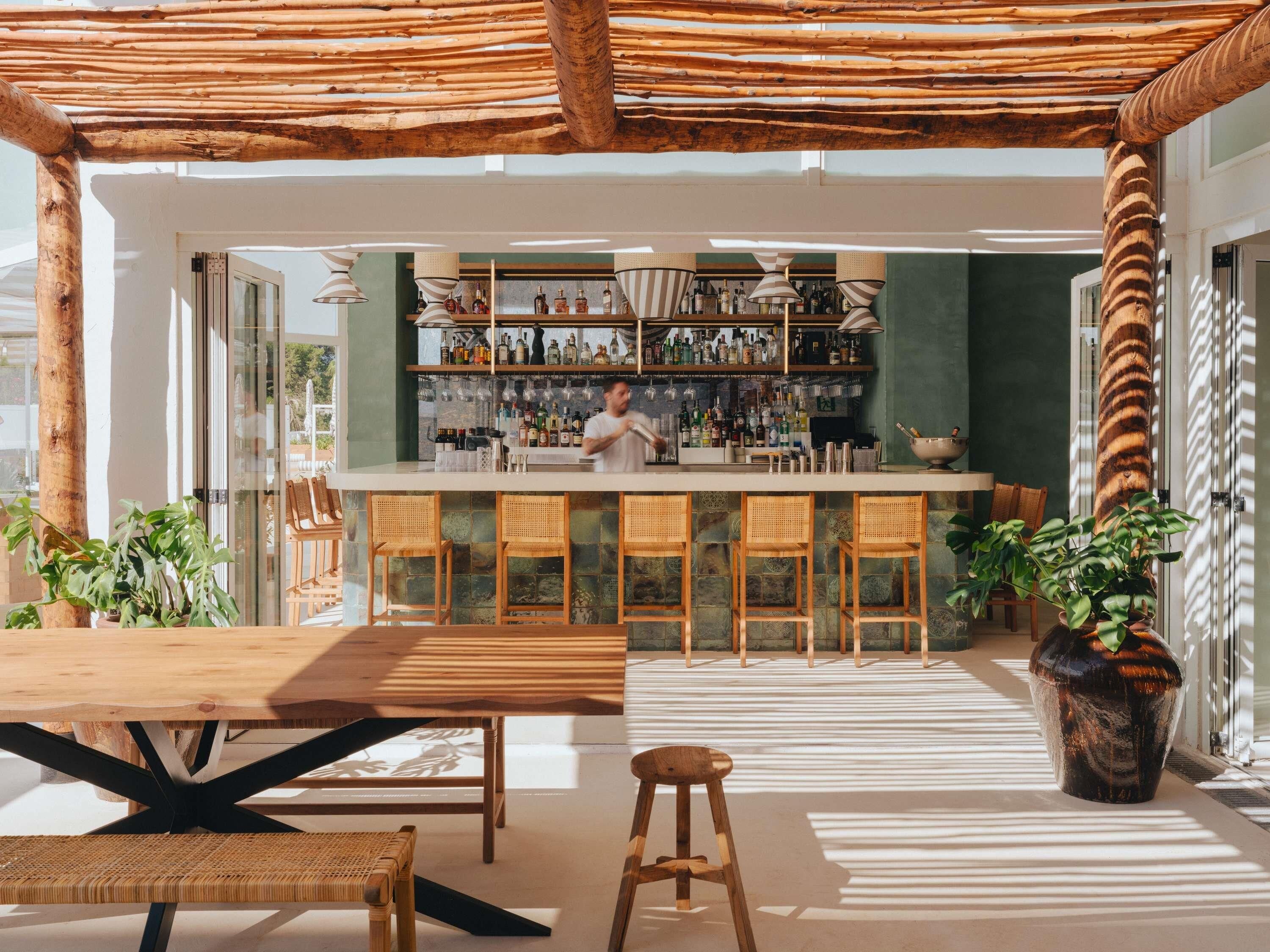 Zona de bar con un cantinero, mobiliario de madera y una variedad de botellas.