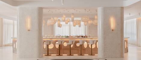 Un bar moderno con barra central, diversas opciones de asientos e iluminación decorativa.