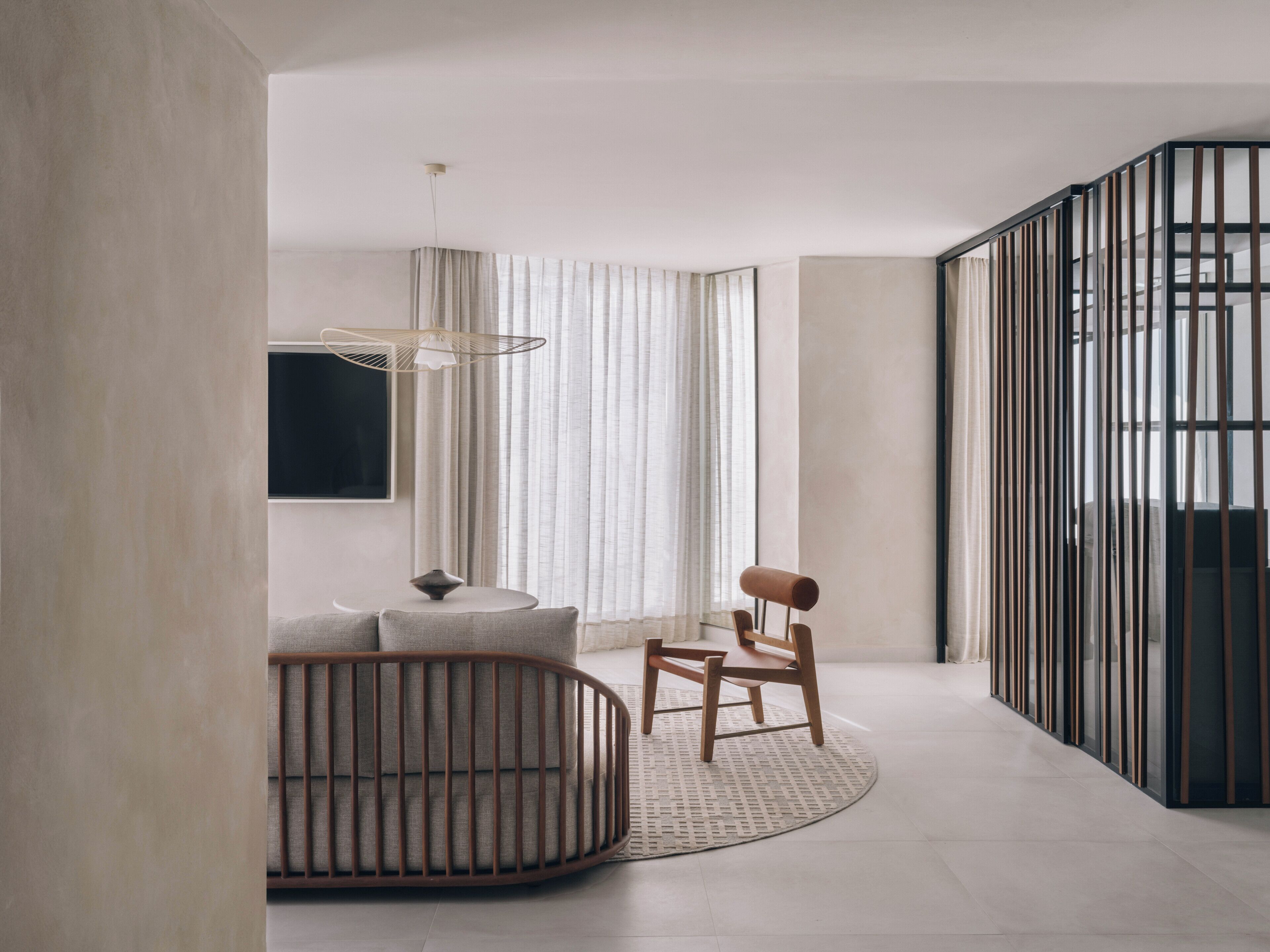 A modern interior with a curved wooden chair, a round table, and a large window with curtains.