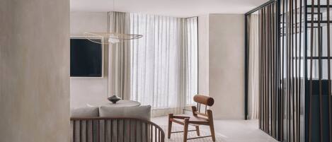 A modern interior with a curved wooden chair, a round table, and a large window with curtains.