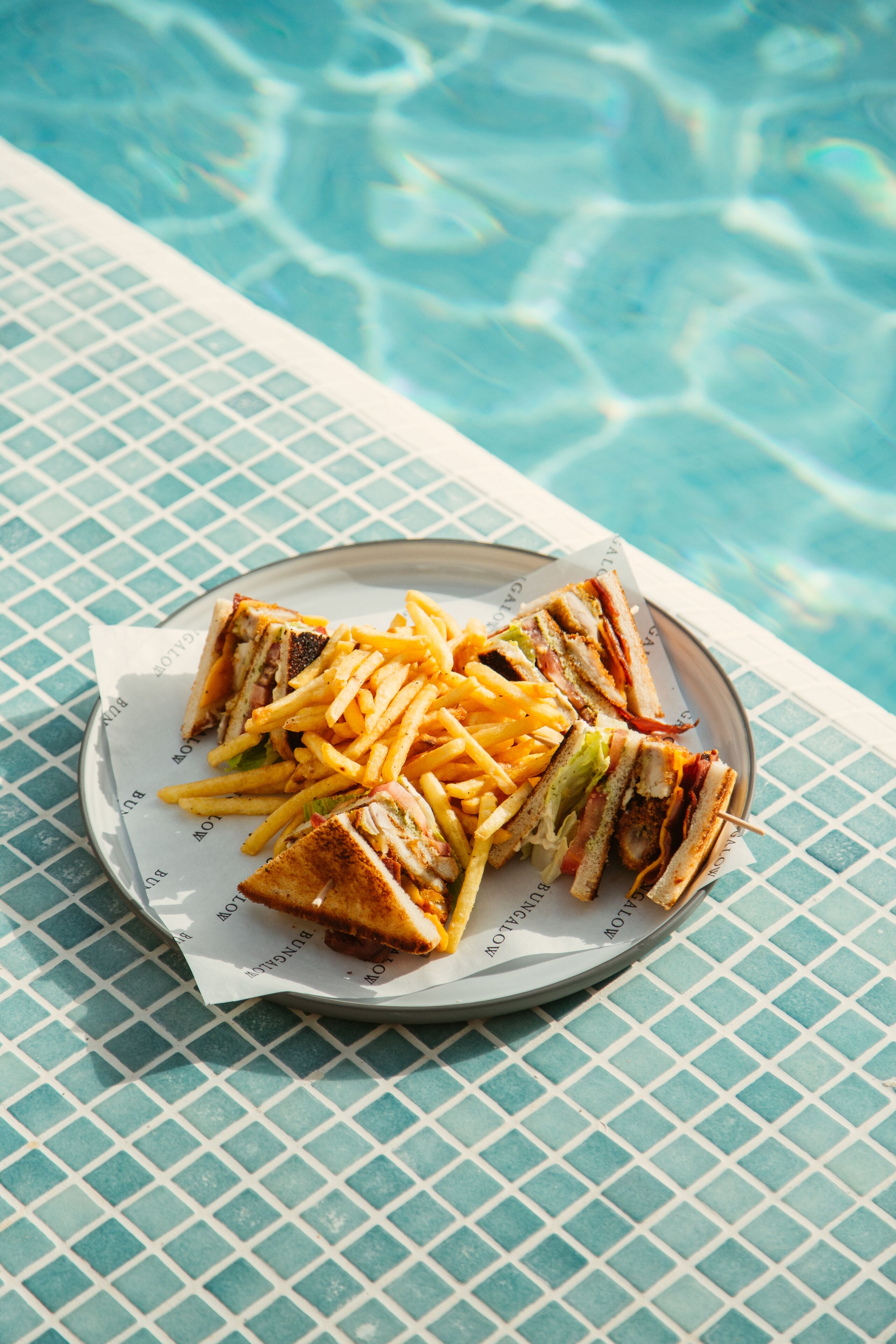 A plate of food with sandwiches and fries by a poolside.