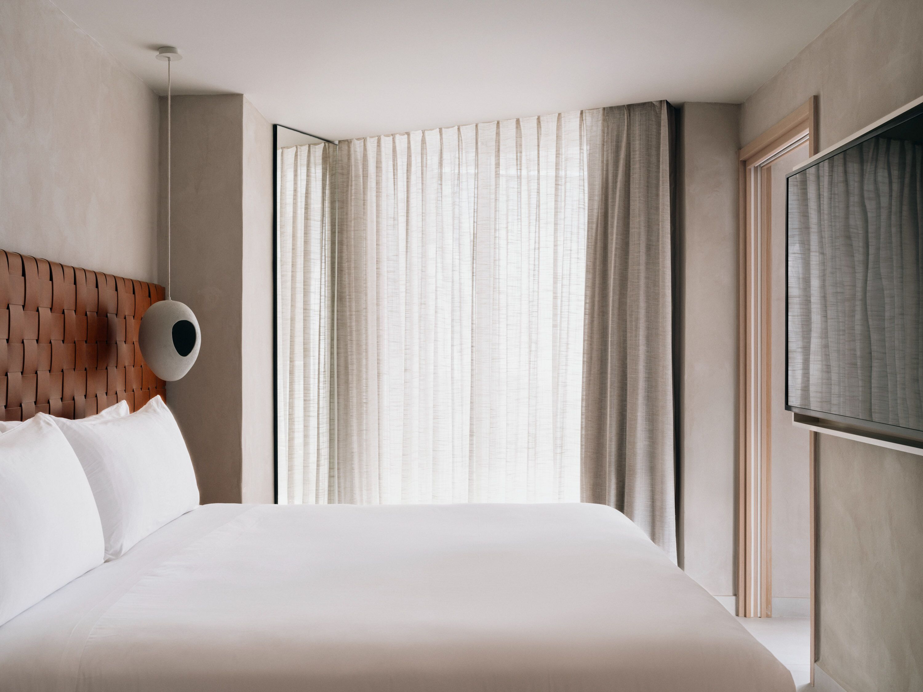 A modern hotel room with a large bed, a round wall-mounted light fixture, and a TV on the wall.