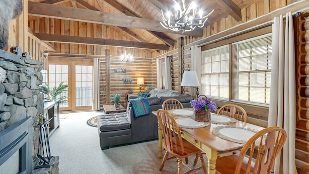 Ein rustikales Holzhaus-Interieur mit Essbereich, Sofa, Kamin und großen Fenstern.
