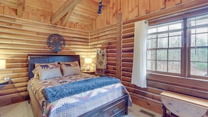 Ein Schlafzimmer in einer Blockhütte mit Bett, Nachttischlampe und einem Fenster mit Vorhängen.