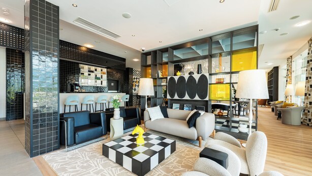 A modern living room with a checkered coffee table, a sofa, and a bar area with shelves and seating. - Ibis Styles Warszawa Airport (Warsaw)