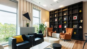 A modern living room with a black sofa, a white coffee table, and a black bookshelf filled with decorative items. - Ibis Styles Warszawa Airport (Warsaw)