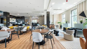 Un comedor moderno con mesas y sillas redondas, una zona de bar y amplias ventanas que aportan luz natural.