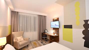 Habitación de hotel con cama, escritorio con computadora, silla y televisor en la pared.