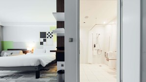 A modern hotel room with a bed, a desk, a shower area, and a view of the outside. - Ibis Styles Warszawa Airport (Warsaw)