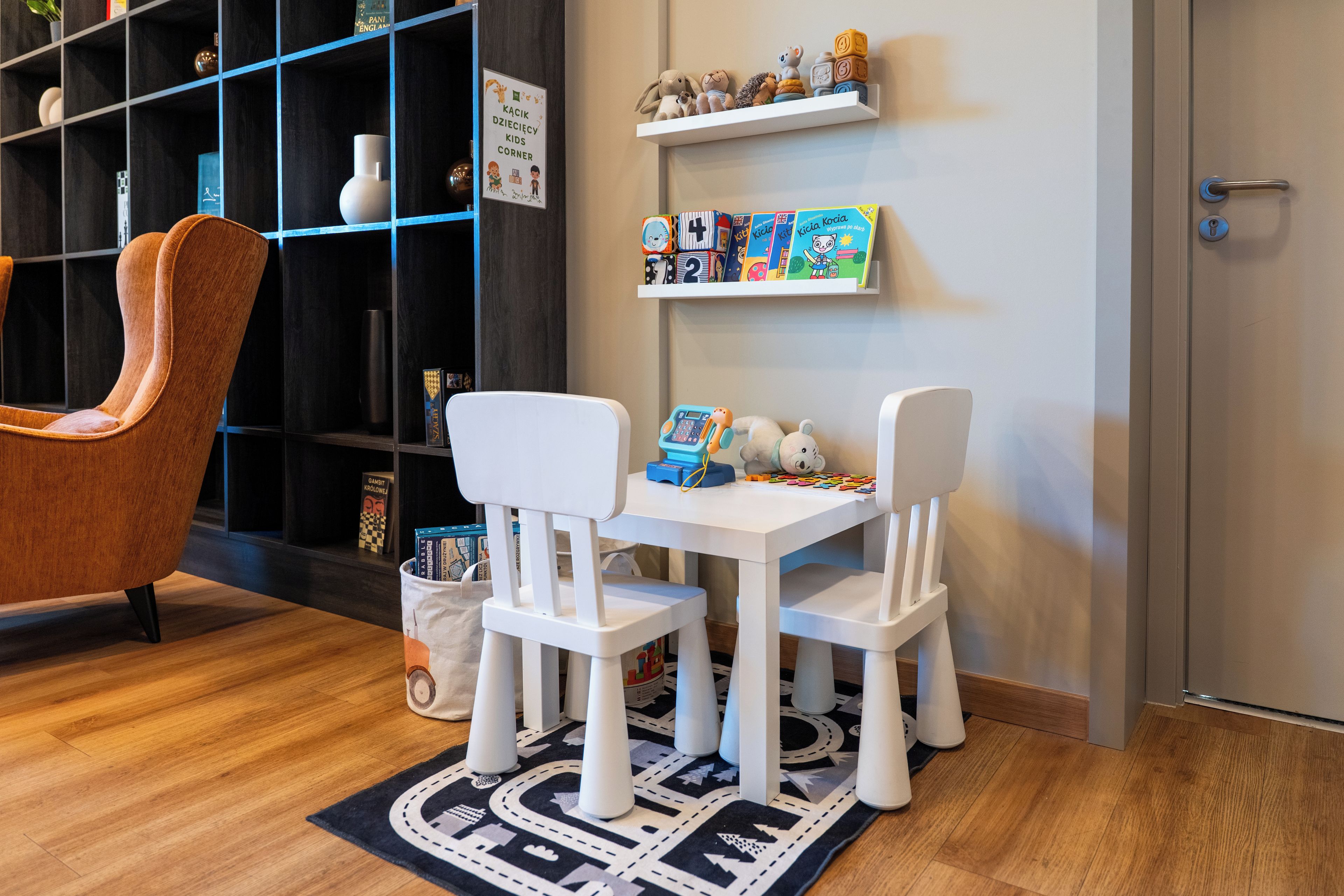 Ein Spielbereich für Kinder mit einem weißen Tisch, zwei Stühlen und einem Teppich mit Straßen- und Auto-Motiv.
