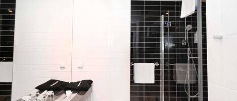 Un baño moderno con un lavabo blanco, una cabina de ducha de vidrio y una pared de ducha con azulejos negros.