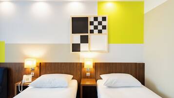 A hotel room with two beds, a wooden headboard, a nightstand with a phone, and a wall-mounted light fixture.