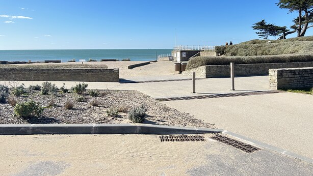 Une promenade en bord de mer, avec un muret en pierre, une colline verdoyante et une vue dégagée sur la mer.
