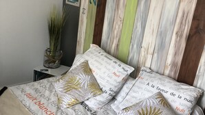 Un lit bien fait, avec une literie à motifs, une tête de lit décorative et une petite table de chevet agrémentée d’une plante.