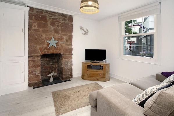 A living room with a brick fireplace, a television on a wooden stand, a sofa, and a window with a view of the street.