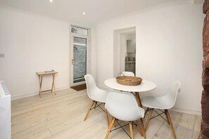 A dining area with a round table, four white chairs, a small side table, and a view through a glass door.