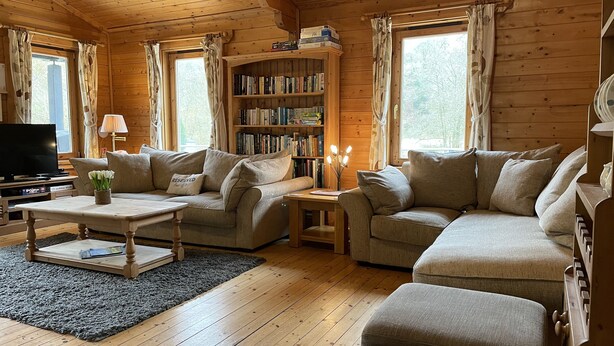 A cozy living room with wooden walls, a sofa set, a coffee table, a bookshelf, and a television. - Valley Lodge (Tiverton)