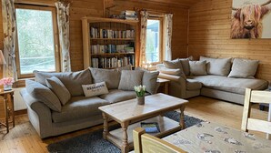 A cozy cabin interior with a grey sofa, a wooden coffee table, and a bookshelf filled with books. - Valley Lodge (Tiverton)