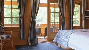 A wooden cabin room with a bed, a chair, a table, and curtains. - Valley Lodge (Tiverton)