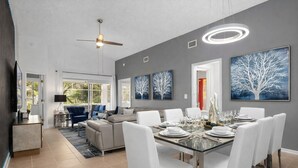 A modern dining area with a glass table, white chairs, and artwork on the walls. - Star Wars Arcade Theater & Private Pool Villa | 3 Kings | Near Disney (Clermont)