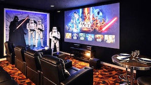 A movie theater with a large screen, reclining seats, a small table with glasses, and Star Wars-themed decorations. - Star Wars Arcade Theater & Private Pool Villa | 3 Kings | Near Disney (Clermont)