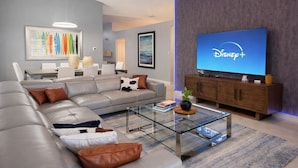 A modern living room with a sectional sofa, a glass coffee table, a flat-screen TV displaying Disney+, and a wooden cabinet. - Star Wars Arcade Theater & Private Pool Villa | 3 Kings | Near Disney (Clermont)