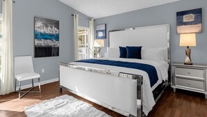 A modern bedroom with a bed, a chair, a nightstand, and artwork on the walls. - Animatronic Dinosaur Villa: 3 King Rooms, Theater & Private Pool Near Disney (Clermont)