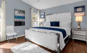 Une chambre à coucher moderne, avec un lit, une chaise, une table de chevet et des œuvres d’art accrochées aux murs.